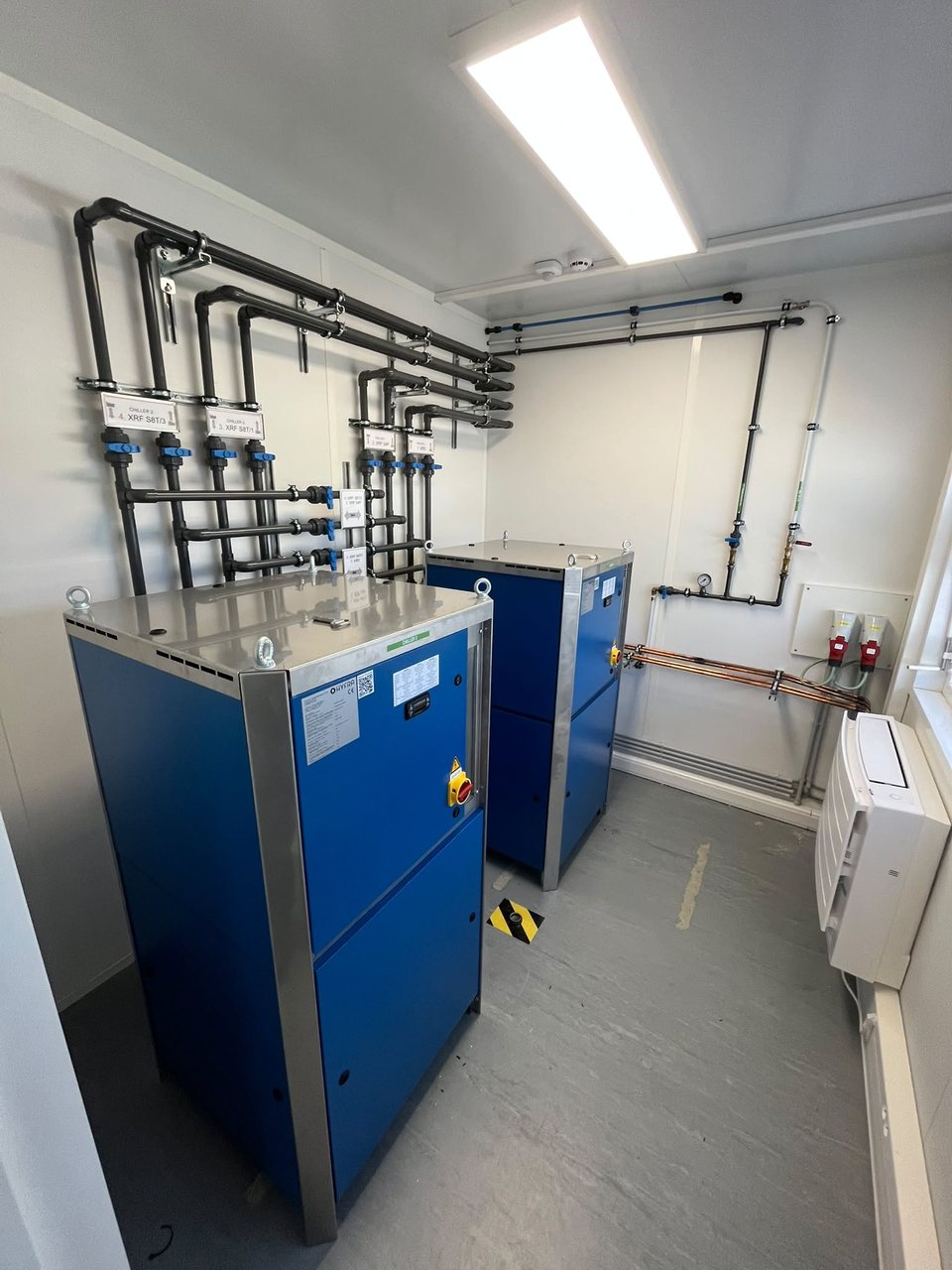 Industriële koelwatercentrale met twee Hyfra-chillers en gelabelde koelwaterleidingen in een technische ruimte, geïnstalleerd door Limko